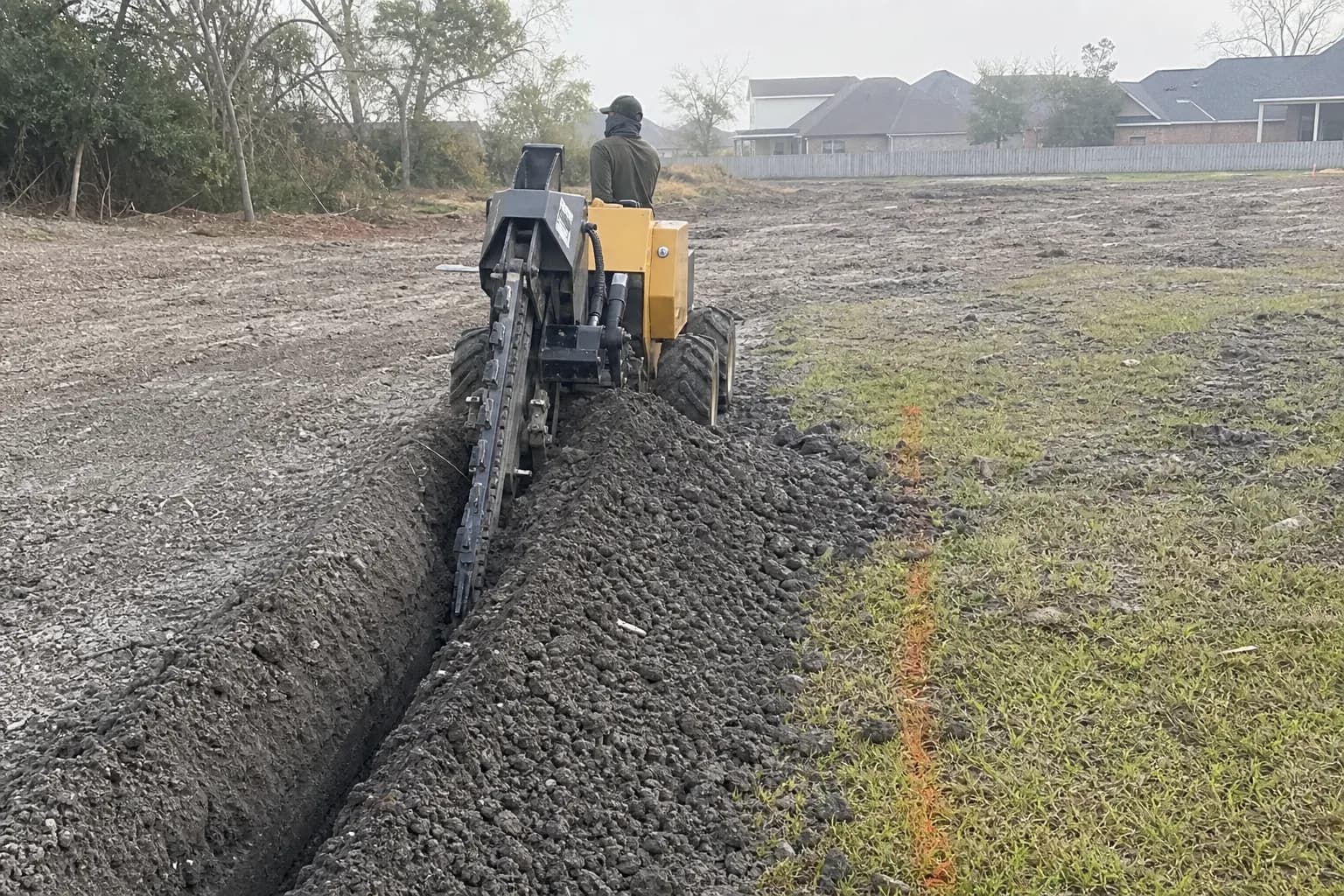 Ride-on trencher cutting a trench along a paint line on a Houston lot
